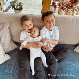Three young boys sitting on a couch, holding a baby.