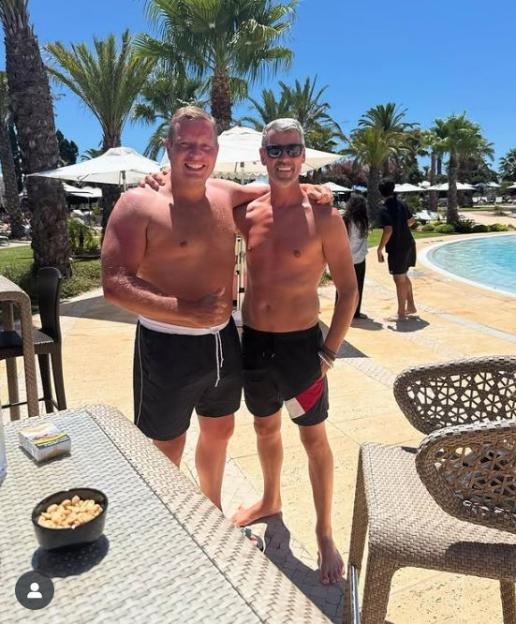 Two shirtless men standing by a pool.