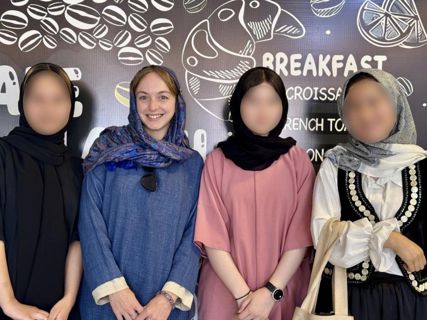 Four women, faces blurred, posing together in front of a breakfast menu.