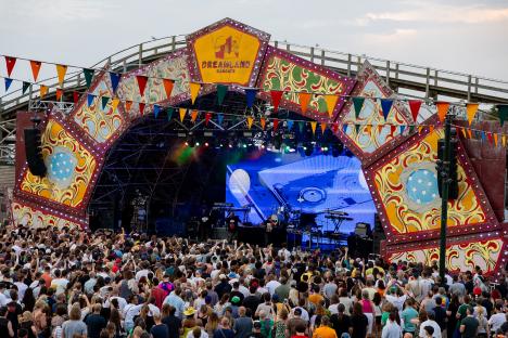 Large crowd at an outdoor concert in front of a stage decorated like a carnival.