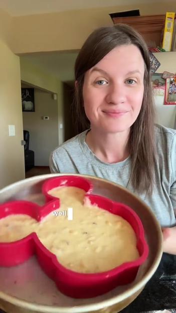 Woman holding Mickey Mouse-shaped cake batter in a baking pan.