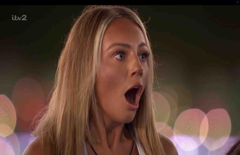 A shocked woman watches on a large screen.