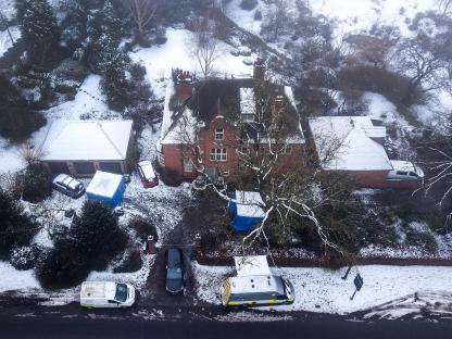 Aerial view of a snow-covered house and surrounding area with police vehicles; crime scene investigation.