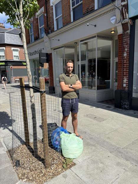 Man standing near bin bags outside a shop, fined for putting bins out too early.