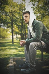A man sits on a bench in a park, looking pensive.