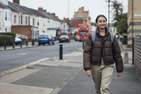 Teenage girl walking along a street in Newcastle upon Tyne, North East England. She is wearing a backpack and is looking ahead of her, smiling. She has braces on her teeth.