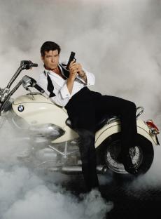 Pierce Brosnan as James Bond on a motorcycle, holding a gun.