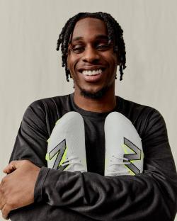 Smiling man holding a pair of white soccer cleats.