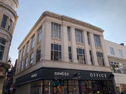 A tan building with large windows and a Newbie and Office storefront.