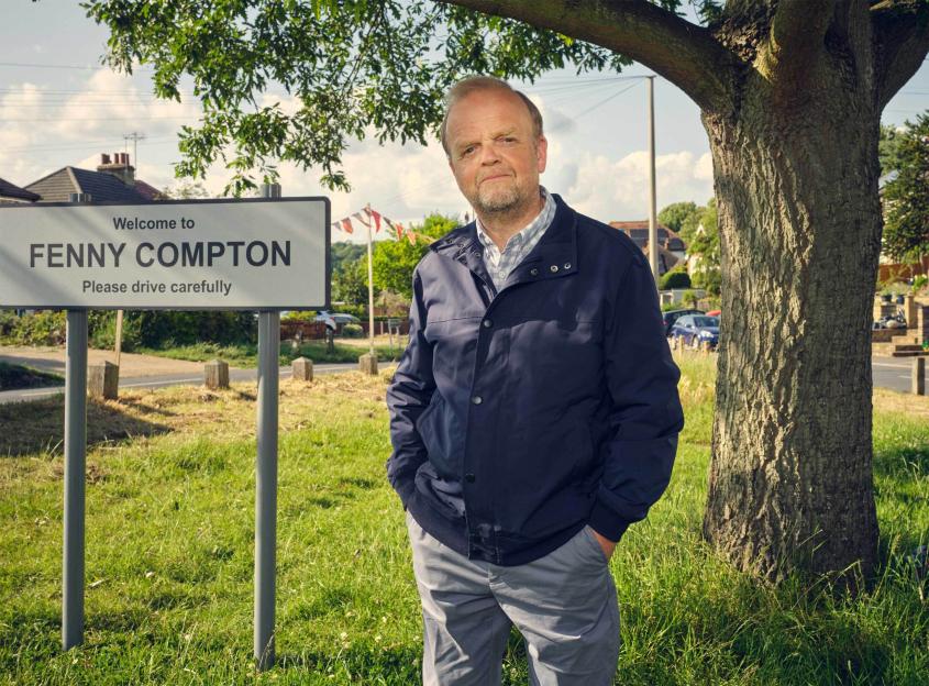 Mr. Bates standing by a Fenny Compton welcome sign.