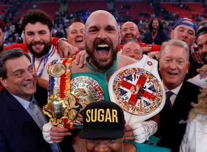 Tyson Fury celebrating a boxing victory with championship belts.