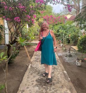 Woman in teal dress walking on a path lined with pink flowers.