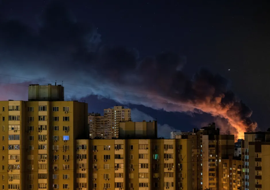 Nighttime view of apartment buildings with a large plume of smoke in the sky.
