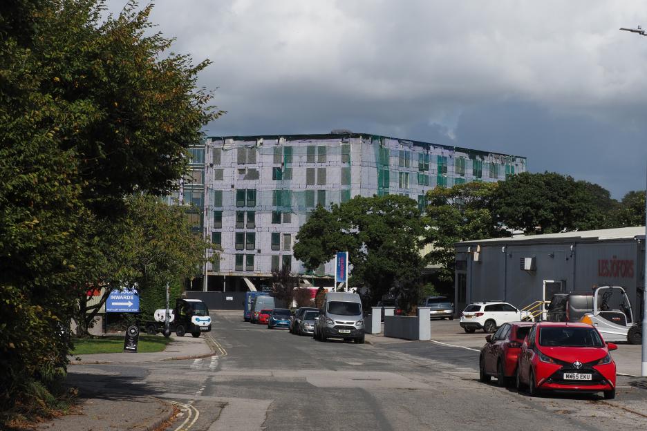 Dilapidated student accommodation building in Penryn, Cornwall, covered in green netting, with a red car parked on the street.