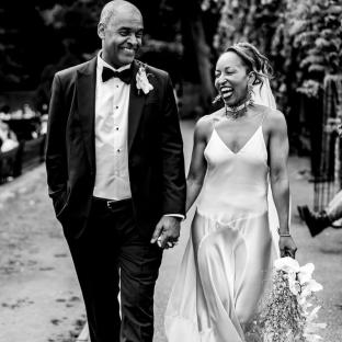 Black and white photo of a bride and groom holding hands and smiling.