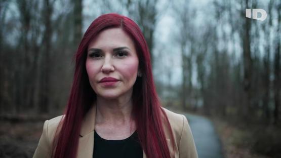 Woman with long red hair, wearing a tan jacket, standing outdoors.