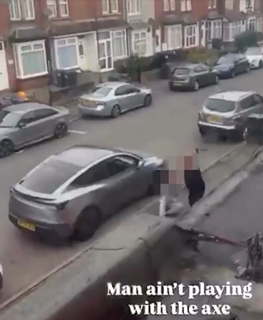 A blurred figure in a street holding an axe near a parked car.