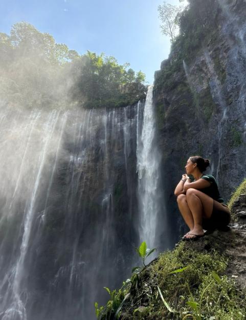 Woman sitting by a large waterfall.