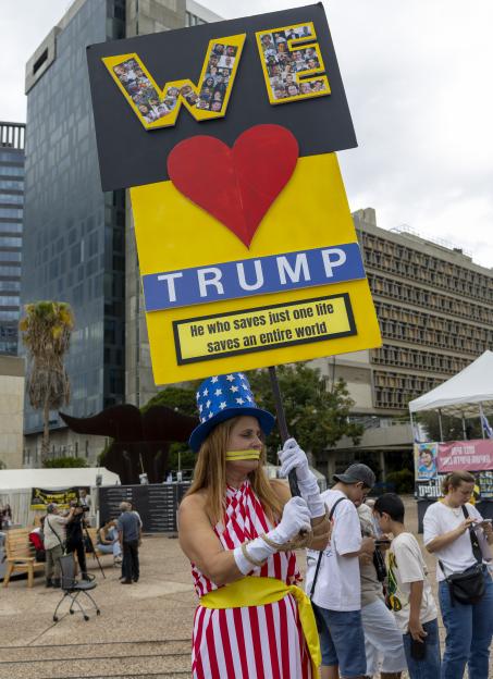 A woman in a patriotic costume holding a sign reading "WE Trump. He who saves just one life saves an entire world."