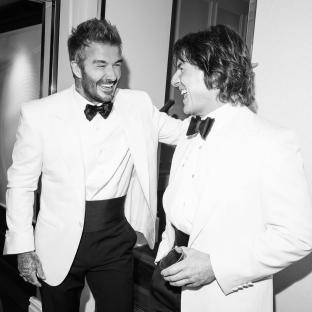 Black and white photo of David Beckham and another man in white dinner jackets laughing together.
