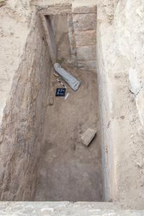 Overhead view of an archaeological excavation site showing a stone statue fragment and other artifacts in the Saqqara necropolis.
