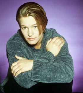 a young man in a blue sweater with his arms crossed