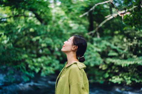 Beautiful young Asian woman meditating in the nature with her eyes closed, setting herself free and feeling relieved. Enjoying fresh air and breathing in the calmness with head up. Freedom in nature. Connecting with nature. Health and wellness concept