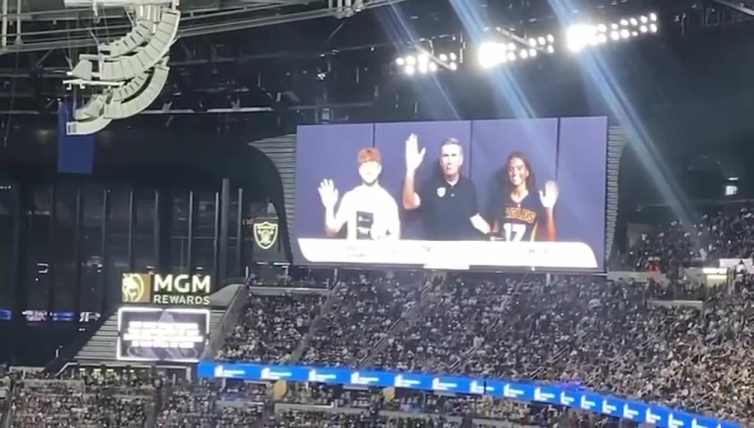 Three individuals waving from a large screen during an event in a stadium.
