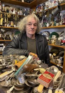 A 76-year-old antique dealer sits amidst his wares.