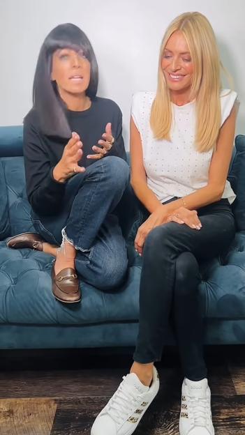 Tess Daly and Claudia Winkleman sitting on a sofa, with Claudia gesturing with her hands.