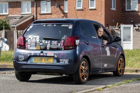 Woman in a car with many bumper stickers, one of which says