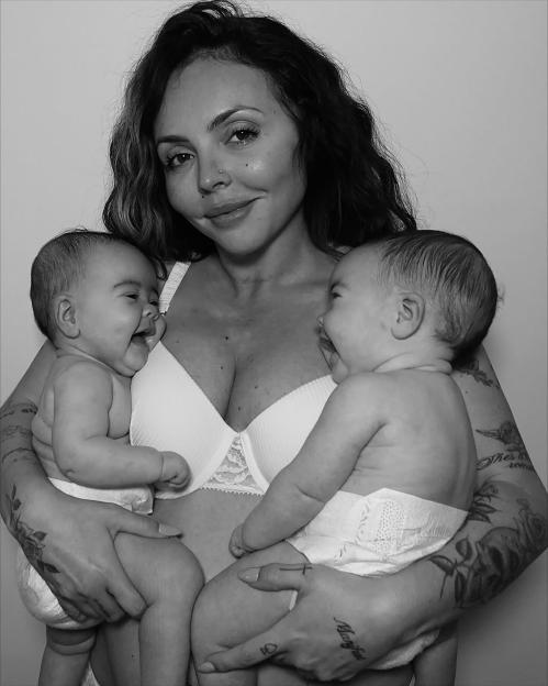 A woman in a bra holding two laughing babies wearing diapers.