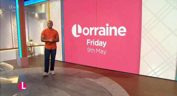 Screenshot of a man standing on a TV show set in front of a pink Lorraine show backdrop.