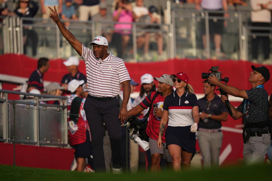 Michael Strahan makes a peace sign as he walks onto the golf course with Miranda Lambert.