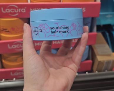Hand holding Aldi's £4.99 Lacura nourishing hair mask, compared to a £28.99 Amika hair mask.