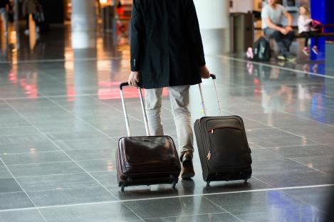 Man pulling two suitcases through an airport.