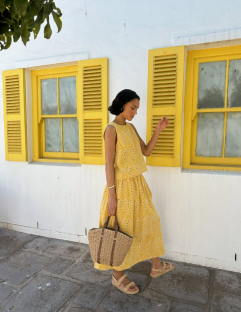 Woman in yellow dress and sandals carrying a straw bag.