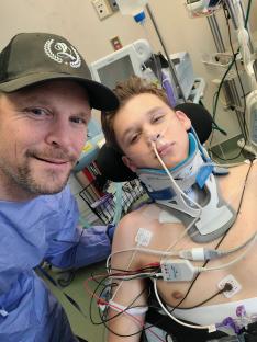 Teenage boy in a neck brace in a hospital bed with his father.