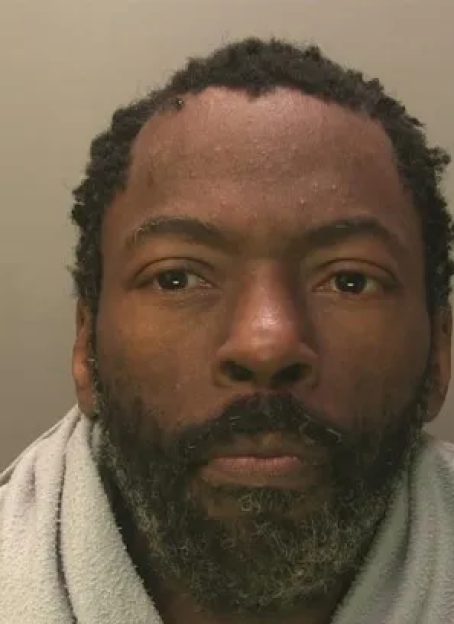 Mugshot of a man with short dreadlocks and a beard.
