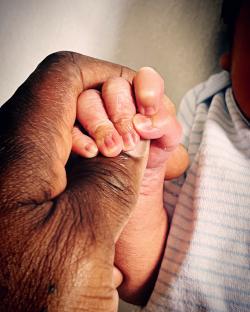 A newborn's hand clasped in an adult's hand.