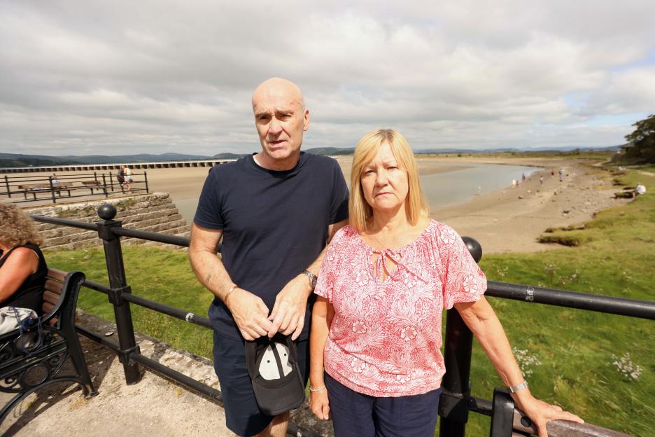 A man and woman stand by a railing overlooking a beach and estuary.