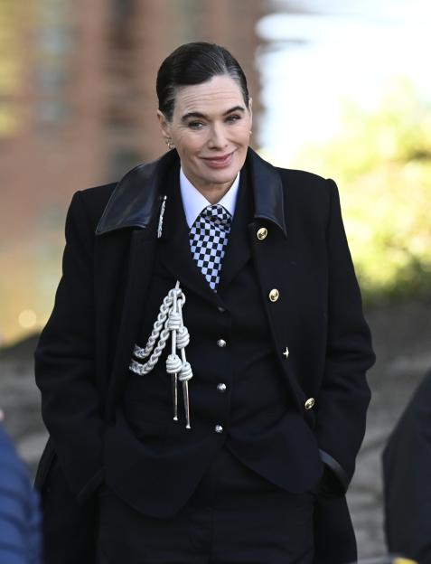 Lena Headey in a black coat and a checkered tie.