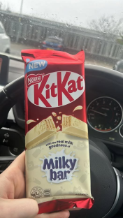A hand holding a KitKat Milky Bar chocolate bar in a car.