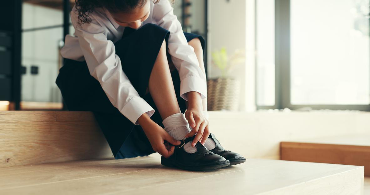 Girl in school uniform tying her shoes.