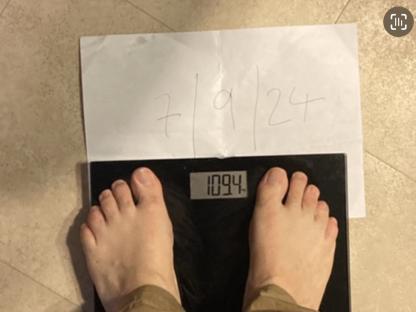 Person's feet on a scale showing a weight of 109.4; a piece of paper shows the dates 7, 9, and 24.
