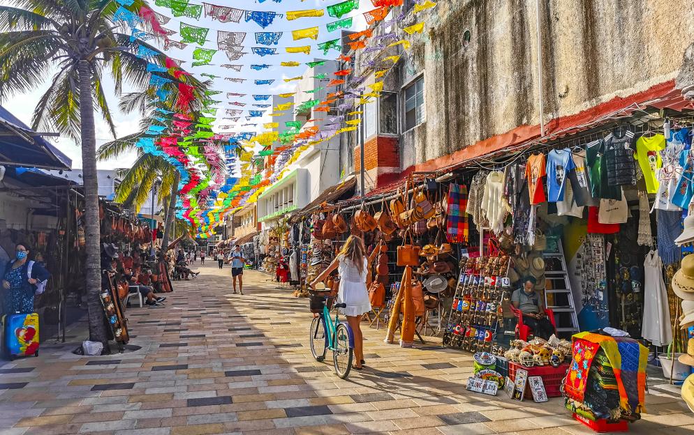 Playa del Carmen street scene with shops, pedestrians, and colorful banners.