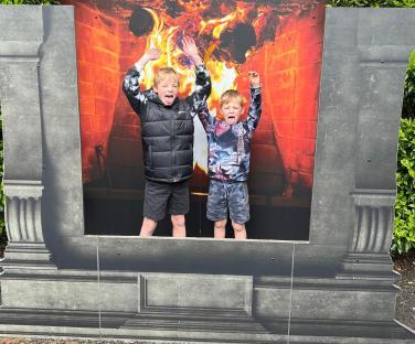 Two boys sticking their tongues out in front of a large fireplace photo cutout at Warwick Castle.