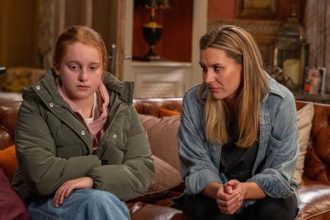 Still image from Emmerdale showing Clemmie (Mabel Addison) and Dawn Fletcher (Olivia Bromley) sitting on a couch.