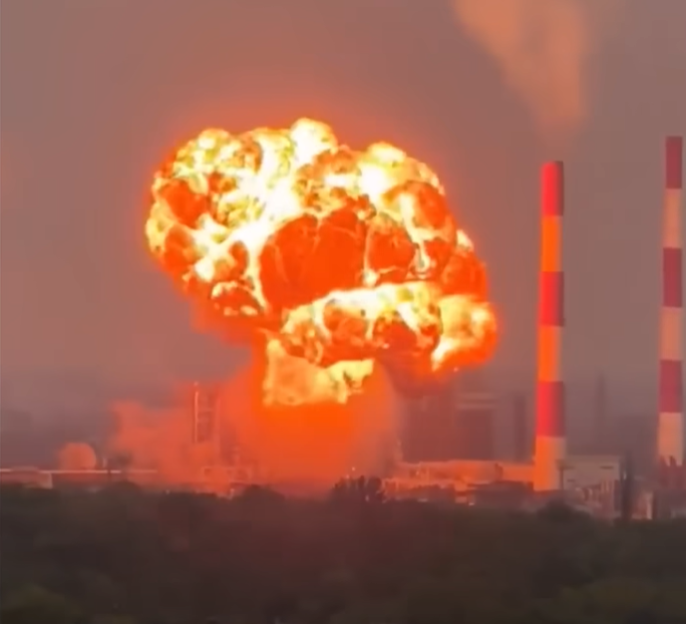Explosion at a power plant with two red and white striped smokestacks visible.
