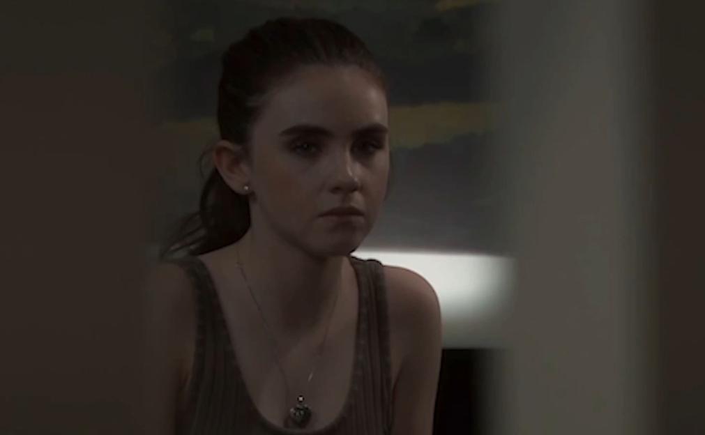 A young woman with dark hair and a serious expression, wearing a tank top and a necklace.